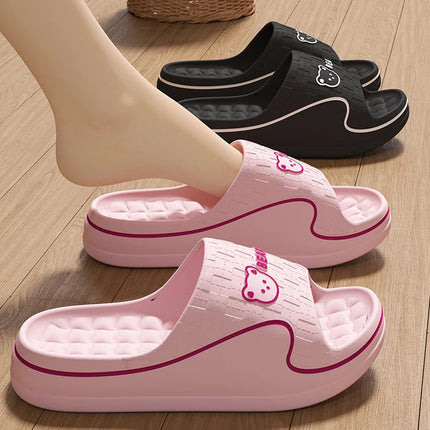 Pink cartoon bear EVA slide slippers worn indoors, with a black pair behind