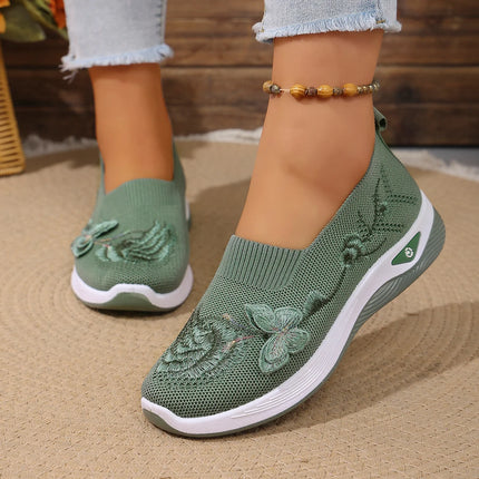 Green knit slip-on sneakers with raised floral details, worn with jeans